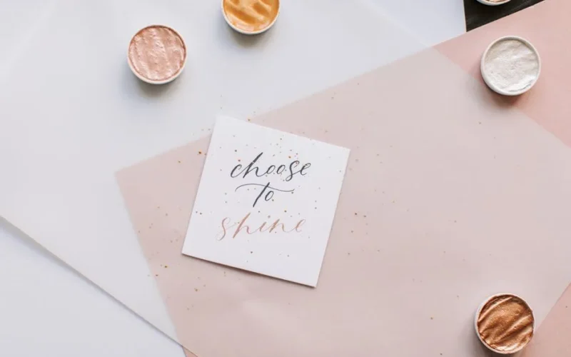 Flat lay of motivational quote 'Choose to Shine' in elegant calligraphy with metallic accents.