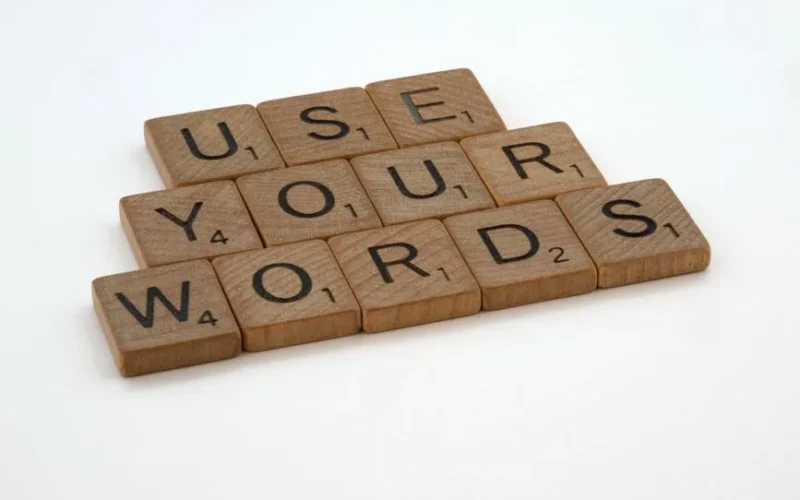 Wooden letter tiles spell 'USE YOUR WORDS' on a white background, promoting linguistic creativity.