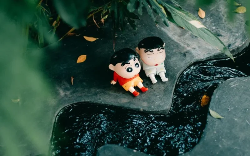 Adorable cartoon dolls sitting near a flowing stream surrounded by lush greenery.