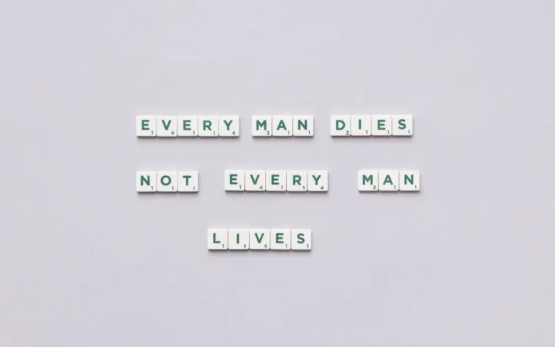 Scrabble tiles spelling 'Every man dies, not every man lives' on gray background.