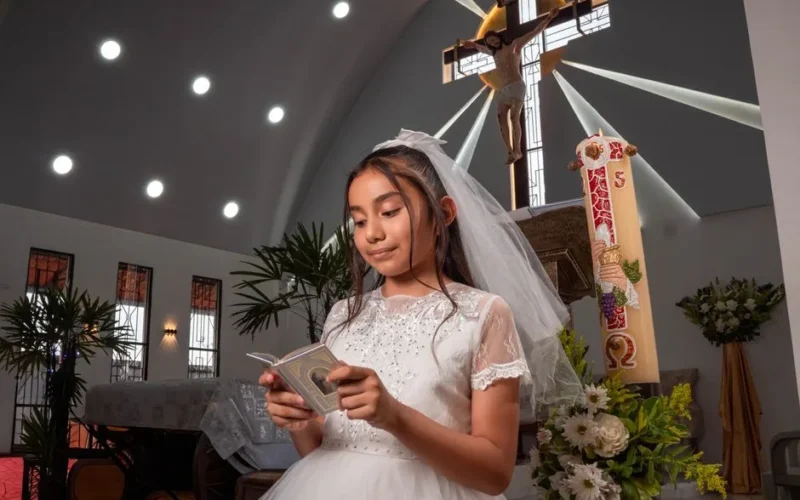 Young girl in white dress reading during communion ceremony in church.