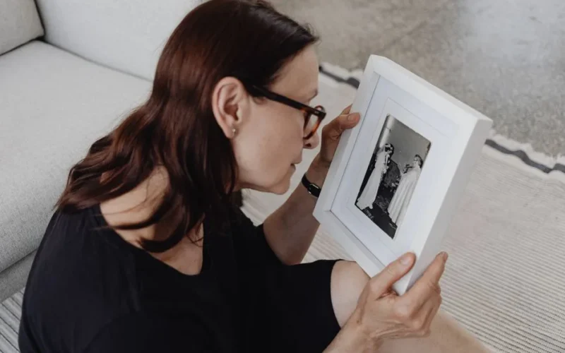 A woman sitting on the floor holding and reflecting on a framed black and white photograph.