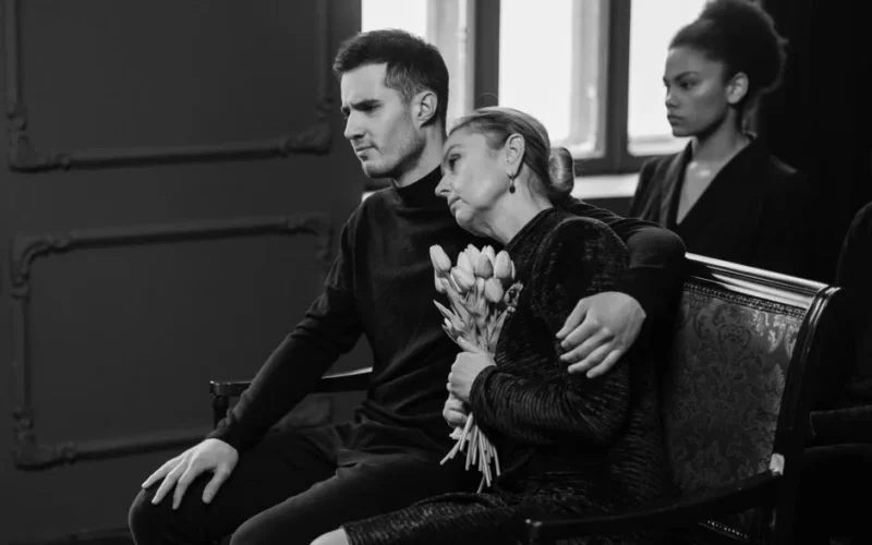 A somber black and white image capturing a grieving family at a funeral.