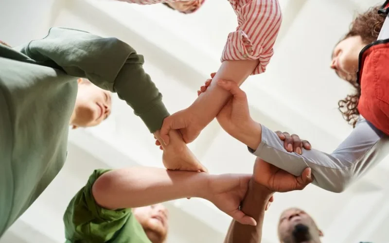 A diverse group of people join hands forming a unity circle, symbolizing teamwork and cooperation.