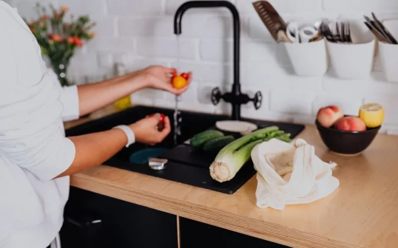 A woman washing fresh vegetables at a kitchen sink in a modern home environment.