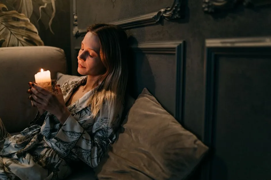 A serene moment of a woman in a robe holding a candle in a calm, dimly lit room.