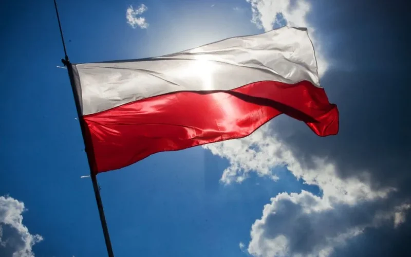 A Polish flag flutters against a bright blue sky with clouds, symbolizing national pride.