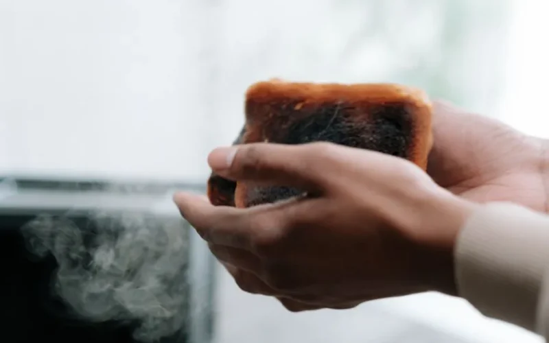 A close-up view of hands holding a toasted slice of bread with visible smoke and burnt texture.