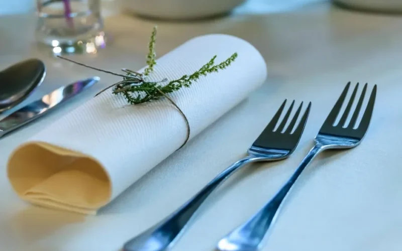 Close-up of a sophisticated table setting featuring a rolled napkin adorned with a sprig and polished silverware.