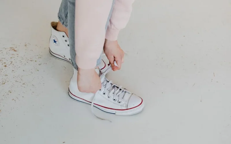 Close-up of a person tying white Converse sneakers, captured from above.