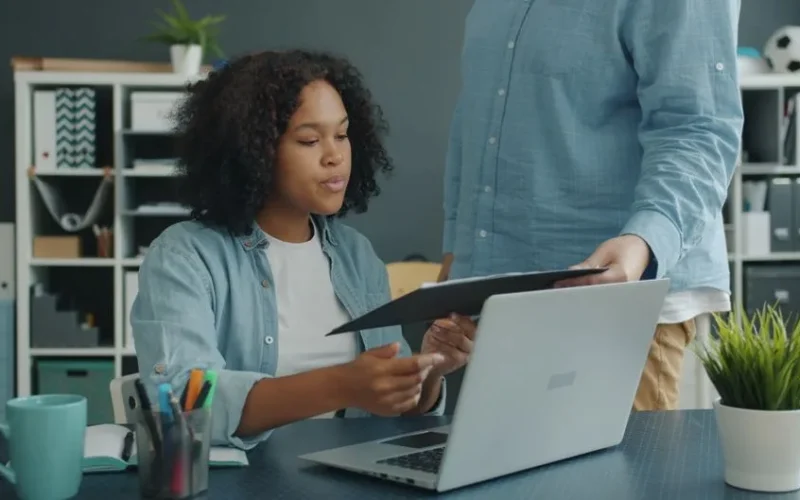 Two professionals collaborating in an office setting with a laptop and documents.