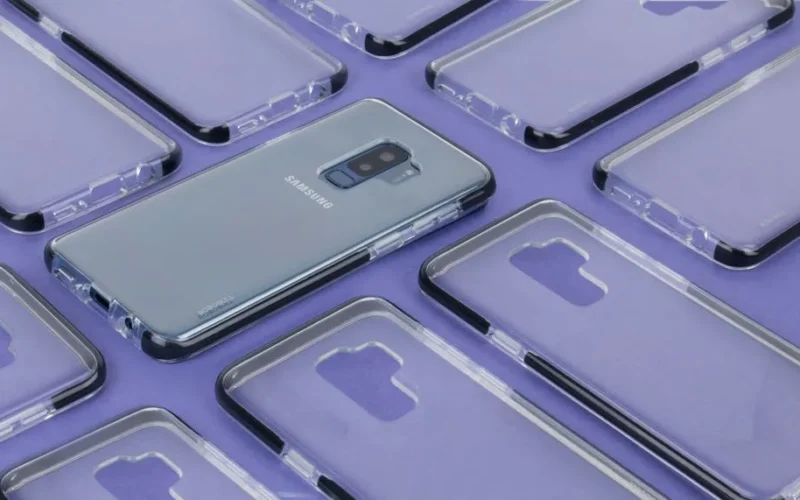 Close-up of a Samsung phone surrounded by transparent cases on a purple surface, showcasing modern technology.