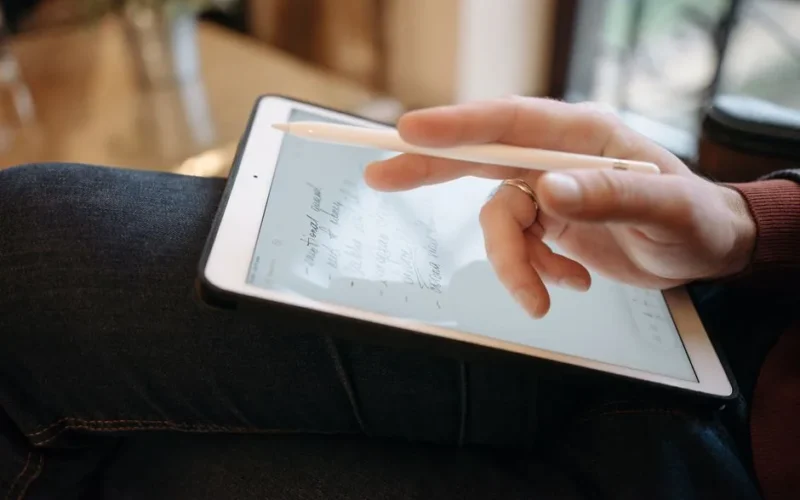 Close-up of a hand holding a stylus, writing on a tablet, featuring handwritten notes. Ideal for digital creativity concepts.