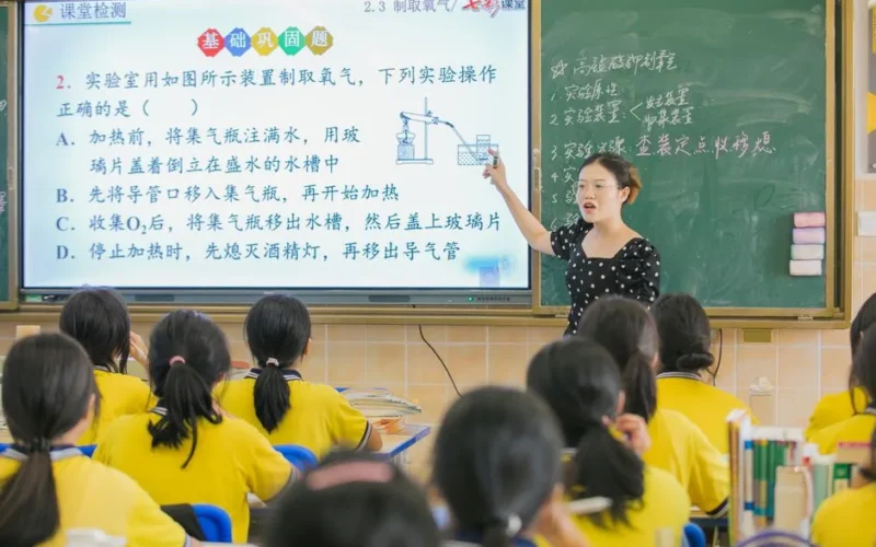 A teacher instructs students in a chemistry class, using a digital board for interactive learning.
