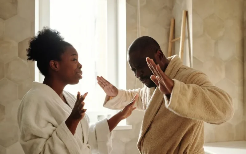 A couple in bathrobes having an emotional discussion in an indoor setting with expressive hand gestures.