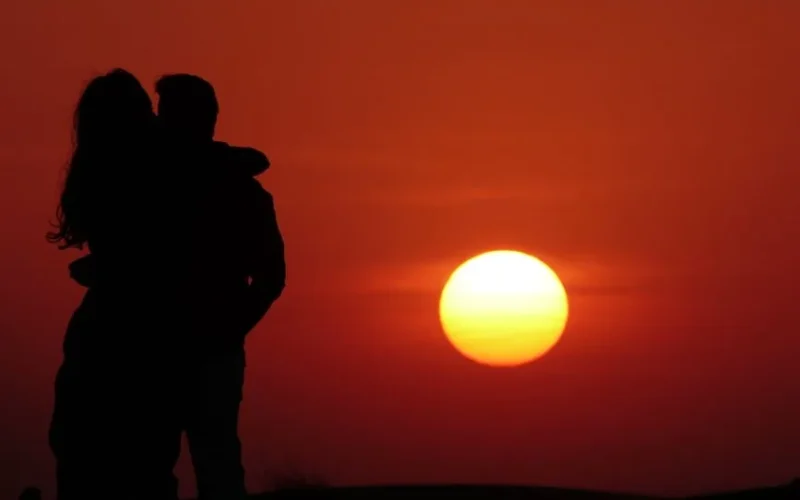 Silhouetted couple embracing during a stunning sunset, evoking romance.