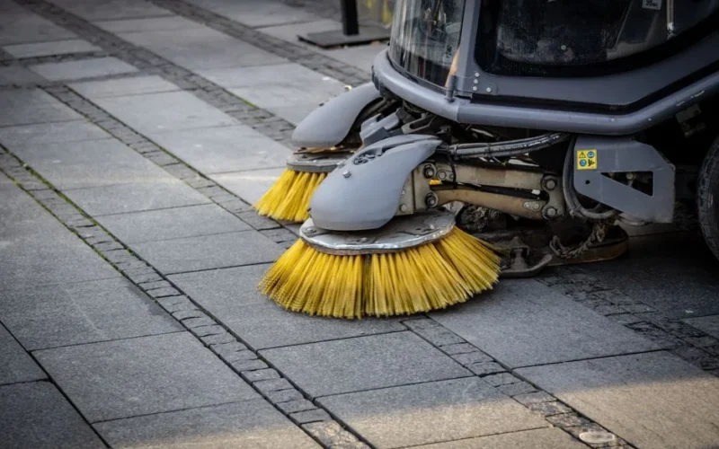 Close-up view of a road sweeper's yellow brushes on a paved street.