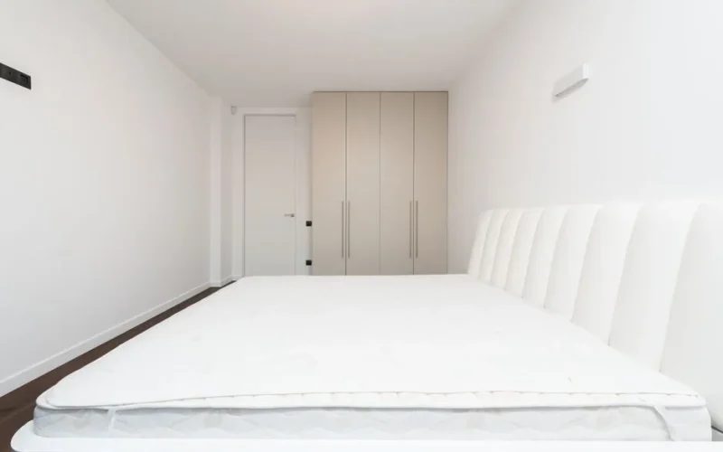 Contemporary minimalist bedroom featuring a white mattress and sleek wardrobe under soft lighting.