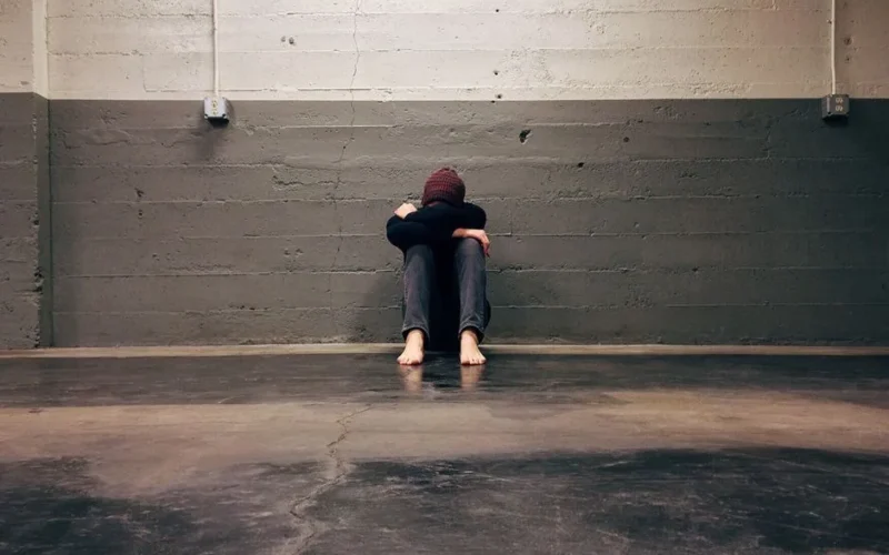 A person sitting alone in a corner, evoking themes of solitude and emotion.