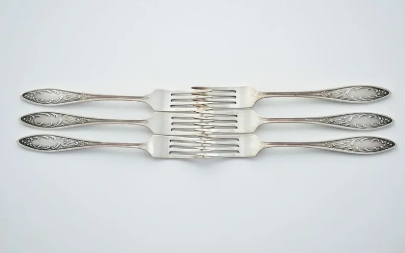 Four intricately designed silver forks arranged on a white surface, showcasing elegant cutlery.