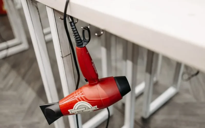 Close-up of a red hair dryer hanging from a white table indoors, showcasing product details.