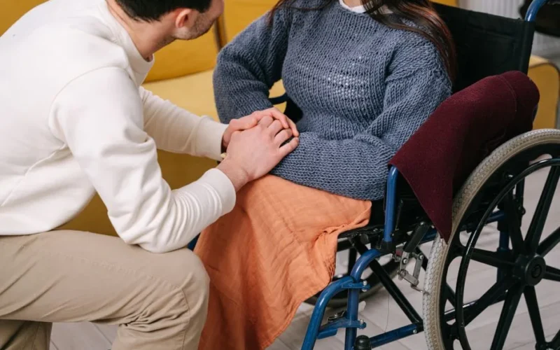 Man providing care and support to woman in a wheelchair indoors.