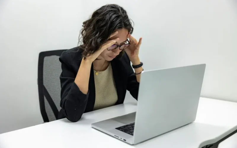 A young woman experiencing stress and fatigue while working on her laptop in an office setting.