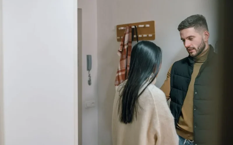 A man and woman talk inside a cozy home. They appear engaged in a conversation.