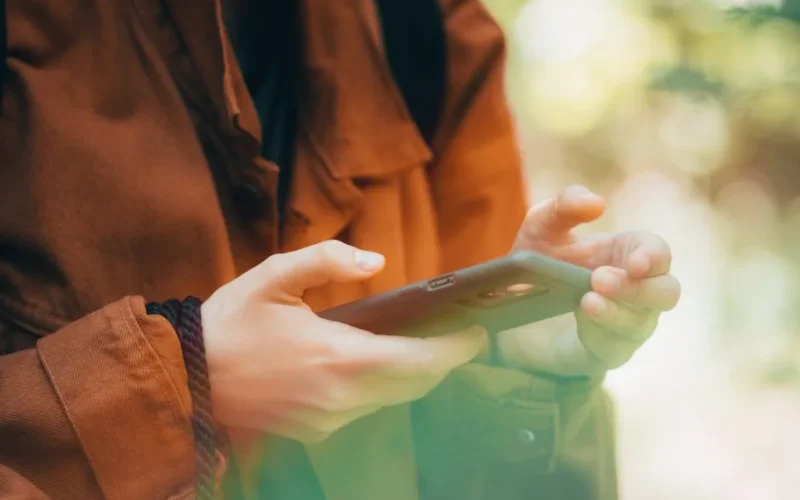 Close-up of hands using a smartphone outdoors with an autumn vibe, showcasing technology and nature.
