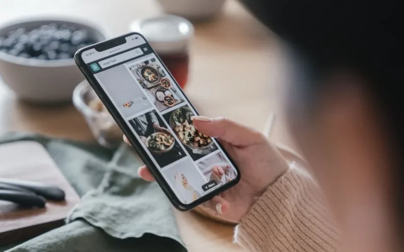 Close-up of a hand holding a smartphone browsing food recipes. Cozy kitchen setting.