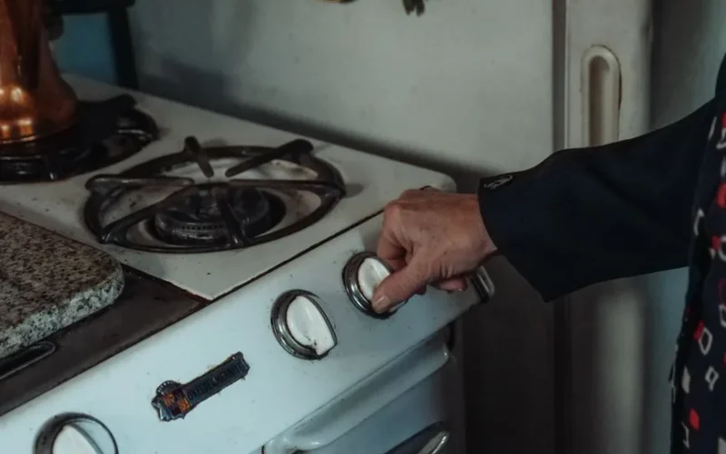 Close-up of a hand turning a knob on a retro gas stove in a home kitchen setting.