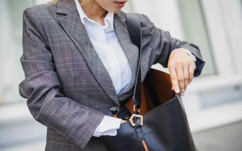 Close-up of a woman in a plaid blazer searching inside a leather bag outdoors.