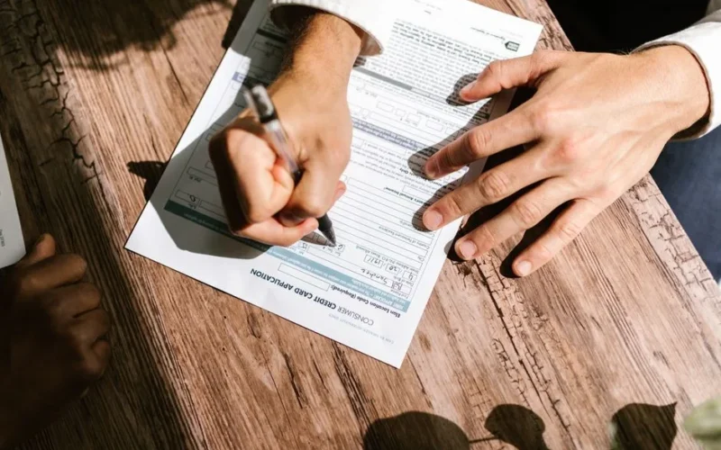 Hands writing on a consumer loan credit application form on a wooden table.