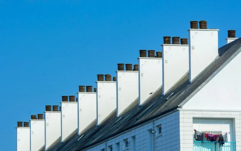 Row of chimneys on modern residential buildings under a clear blue sky. Urban architecture with rooftops.