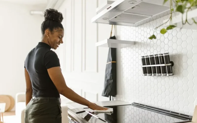 A woman cheerfully cleans her kitchen, focusing on the electric stove in a bright, modern space.