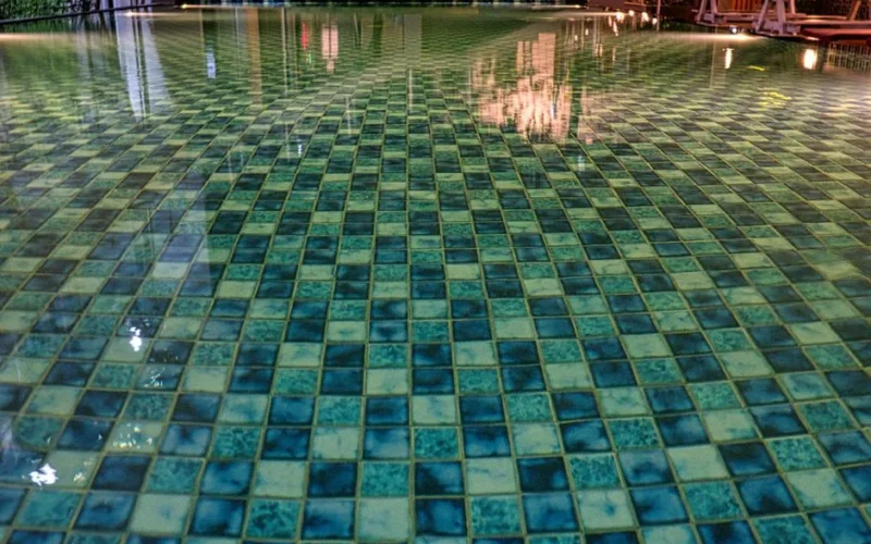 Swimming pool with blue tiles under constructions reflecting in shiny transparent aqua in daytime