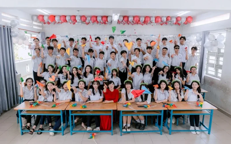Group of students celebrating indoors with balloons and paper planes.