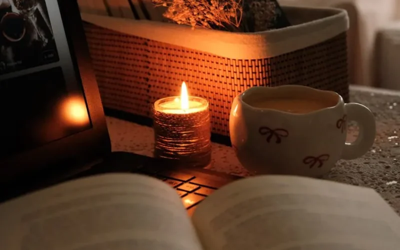 Warm and cozy evening scene with candlelight, a cup of drink, and an open book.