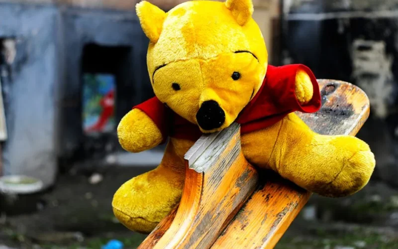 A close-up of a yellow stuffed bear toy on a wooden seesaw outdoors in L'viv, Ukraine.