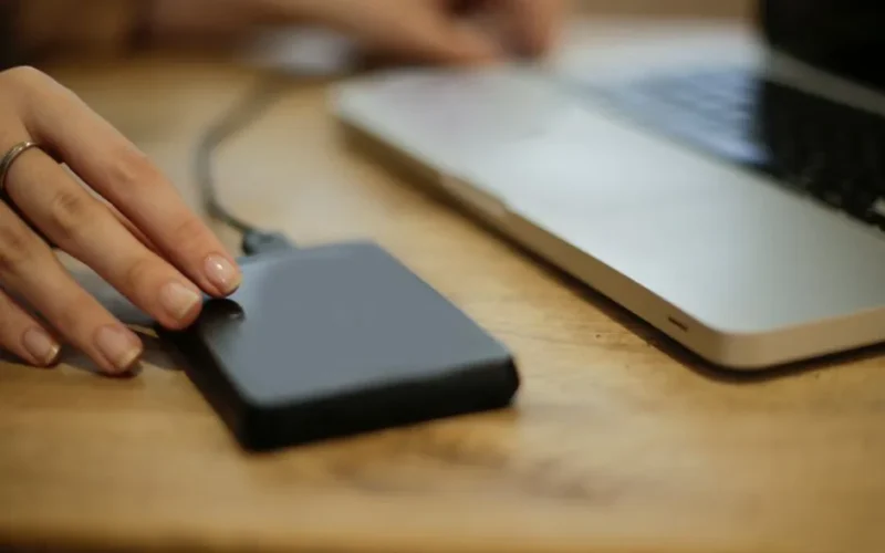 Close-up of a person connecting an external hard drive to a laptop on a desk.