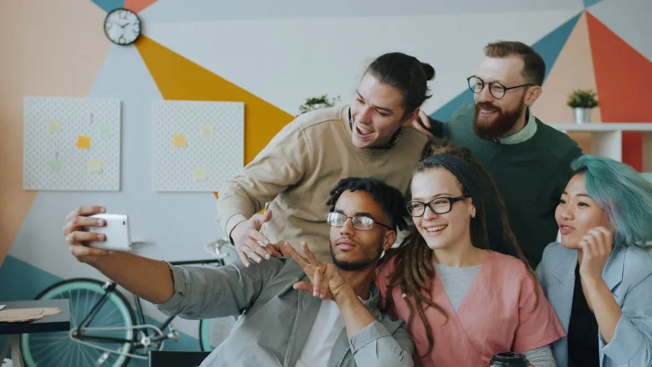 Radosna zróżnicowana grupa przyjaciół robi sobie selfie w pomieszczeniu na tle kolorowej nowoczesnej dekoracji